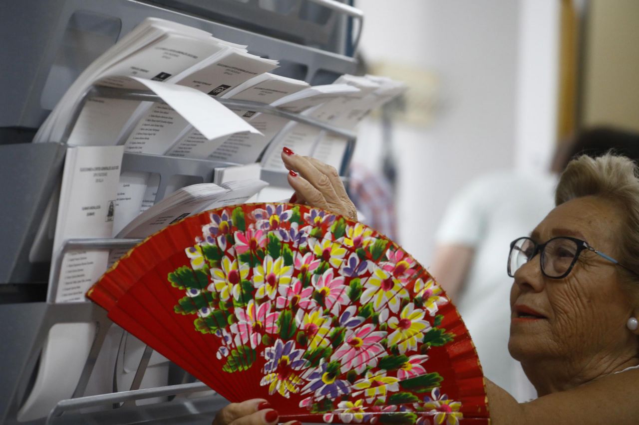 Una mujer con abanico elige una papeleta para ejercer su derecho al voto en el Colegio Miguel de Cervantes de Écija (Sevilla)