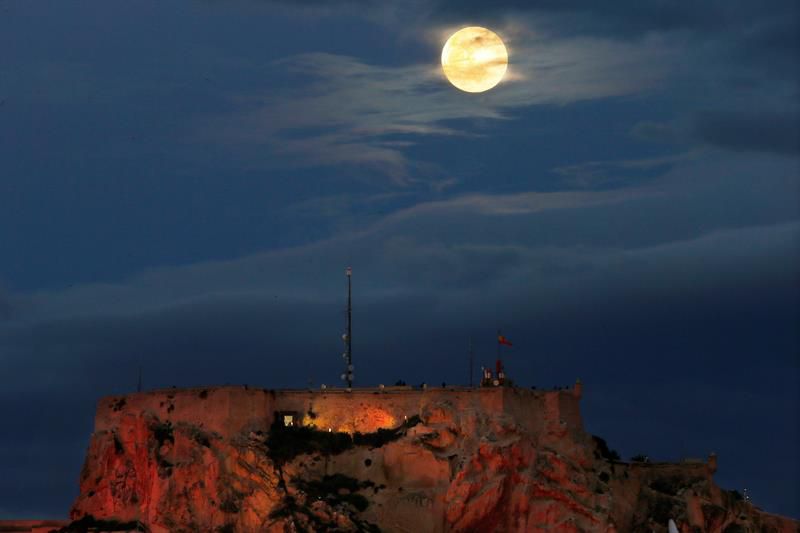 La luna llena asoma entre las nubes, por encima del Castillo de Santa Bárbara de Alicante.