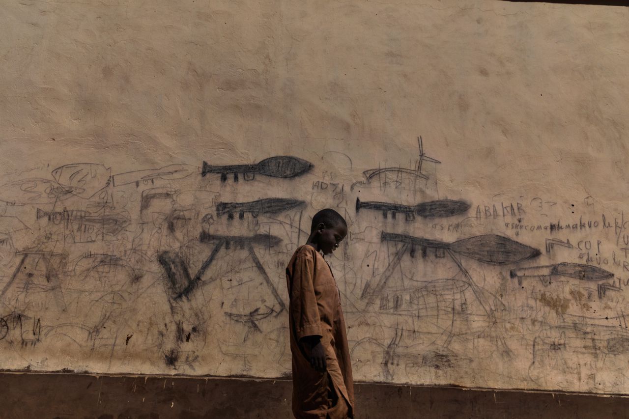 Un niño huérfano pasa junto a una pared con dibujos que muestran lanzadores de granadas propulsados ??por cohetes en Bol, Chad.