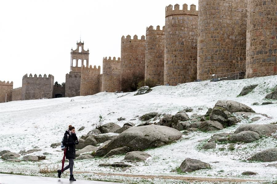 Una mujer camina junto al lienzo norte de la muralla de Ávila cubierta por una fina capa de nieve caída en las últimas horas.