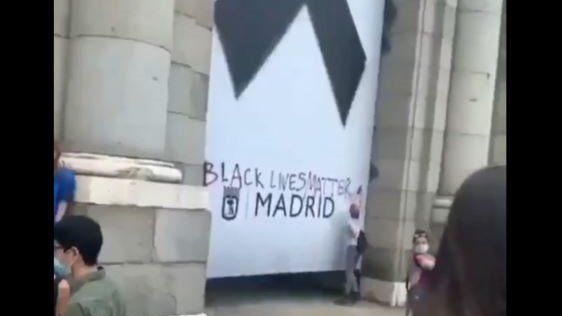 Una manifestante antirracista vandaliza el crespón negro de Madrid en memoria de las víctimas del Covid-19