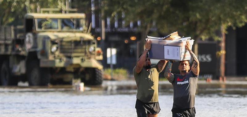  Dos hombres llevan sus pertenencias mientras atraviesan el agua como consecuencia de las inundaciones por el paso del huracán Harvey en Houston.