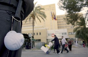 Un guardia de seguridad, con una mascarilla colgada junto a la porra, del hospital universitario 